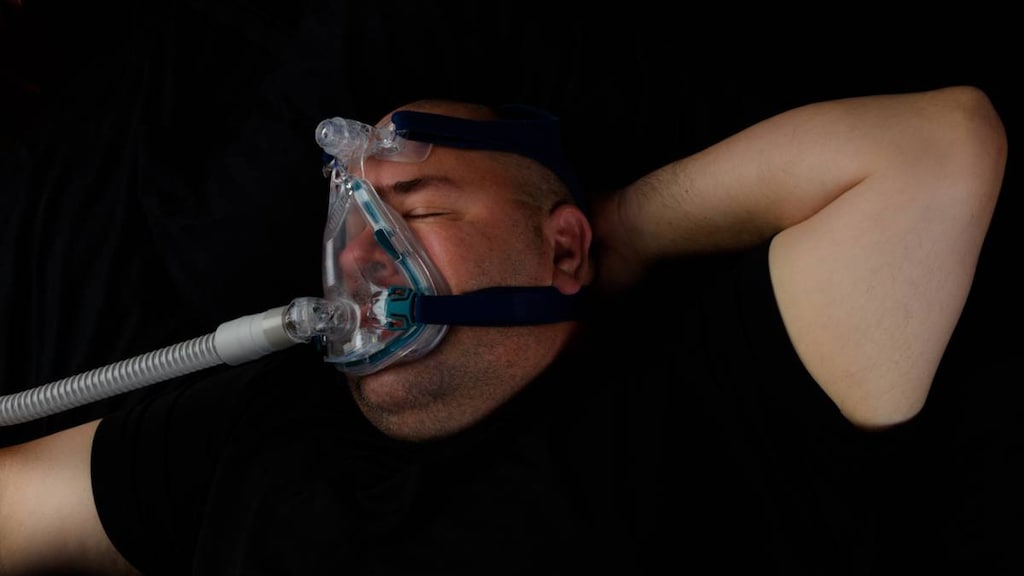 Overweight man using CPAP machine while sleeping.