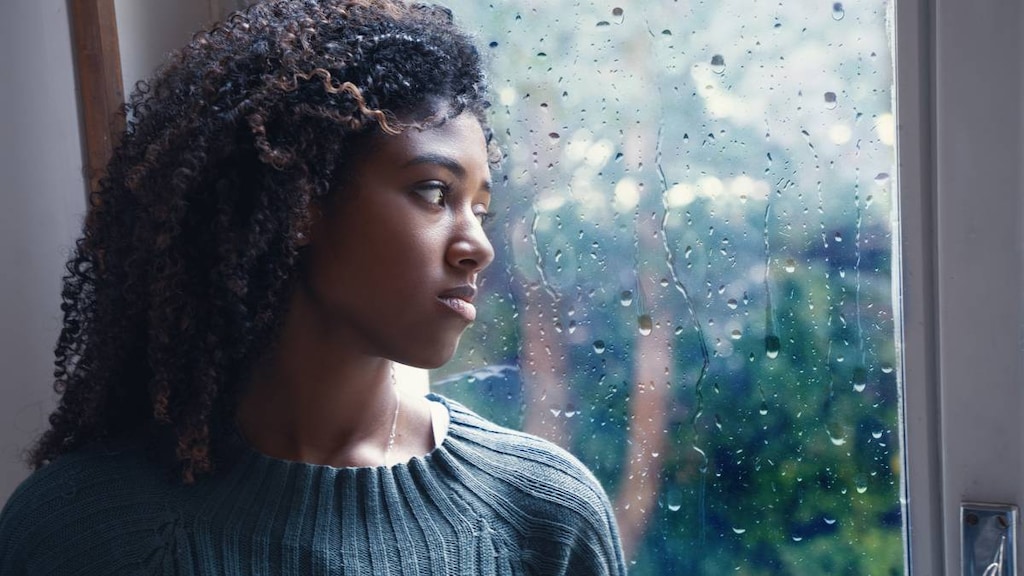 Woman with seasonal affective disorder (SAD) stares out into the cold and rain.