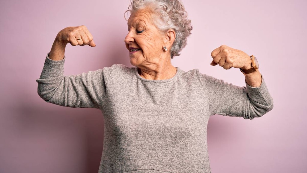 Senior beautiful woman wearing casual t-shirt standing over isolated pink background showing arms muscles smiling proud. Fitness concept.