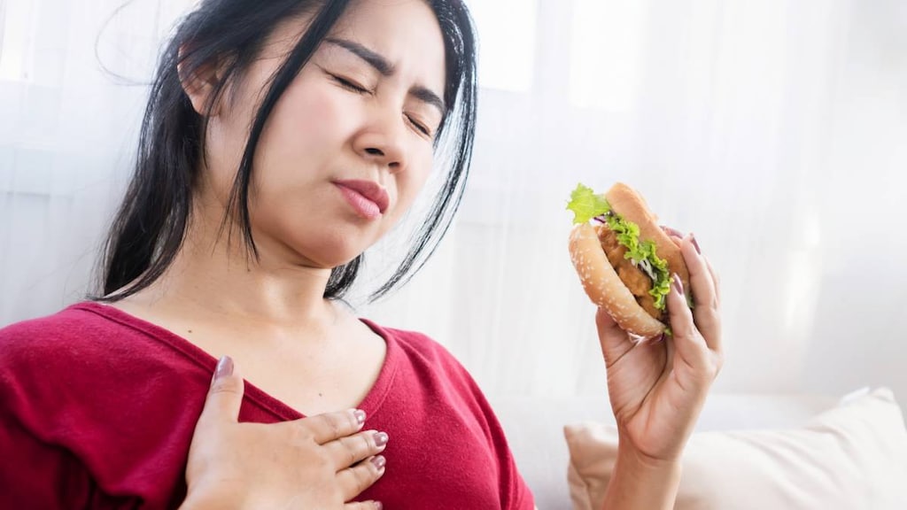 Asian woman with heartburn (acid reflux) after eating burger.