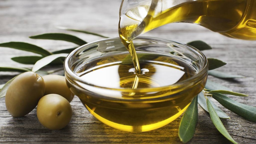 Bottle pouring virgin olive oil in a bowl close up.