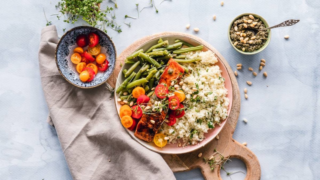 Plate with Salmon, quinoa, tomato, beans and seeds on a board displaying foods that help to lower cholesterol