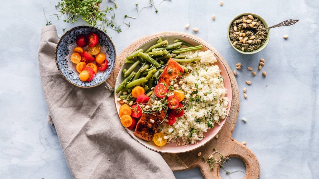 Plate with Salmon, quinoa, tomato, beans and seeds on a board displaying foods that help to lower cholesterol