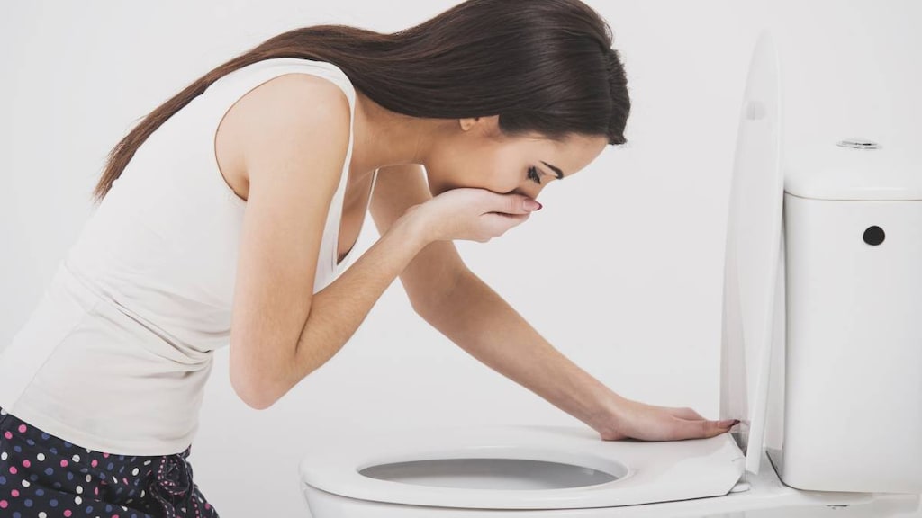 Young woman with morning sickness leaning over toilet bowl.