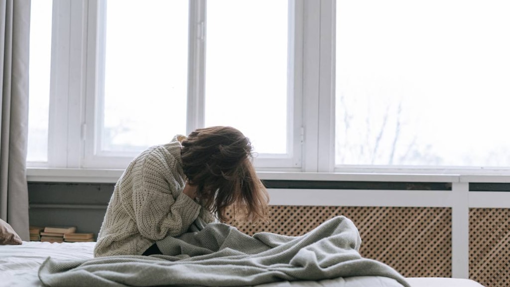 woman sitting on a bed with head in her hands.image credit Ivan Samkov.image