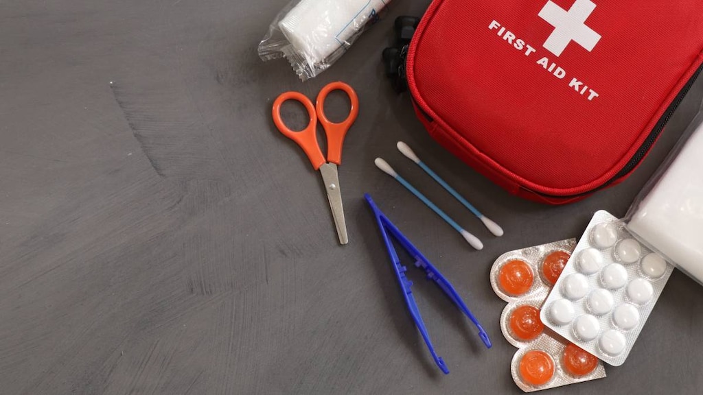 Red first aid kit with tweezers, scissors and medical items around it.