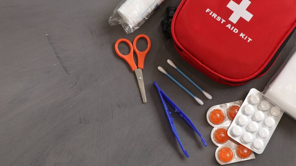 Red first aid kit with tweezers, scissors and medical items around it.
